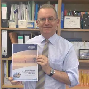 Man in an office holds a report titled 'Environmental Health Inequalities in Europe.'