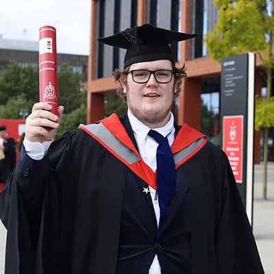 Joshua Lockley in his graduation cap and gown holding a scroll