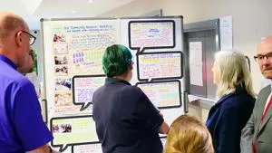 Several people gather around a colourful research poster displayed on a screen.