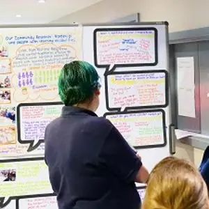 Several people gather around a colourful research poster displayed on a screen.