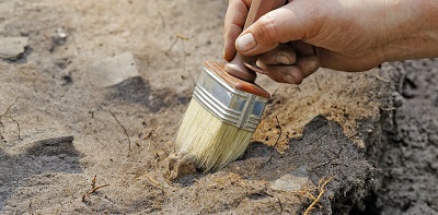 A hand pictured brushing away earth from an archaeological dig
