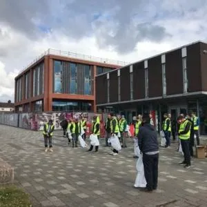 Volunteers in high-visibility vests gather outside a campus building for a litter pick.