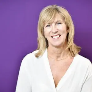 Smiling blonde woman in a white blouse poses against a purple studio background.