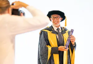 Lloyd Cooke in his graduation cap and gown holding a scroll