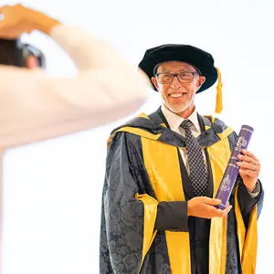 Lloyd Cooke in his graduation cap and gown holding a scroll