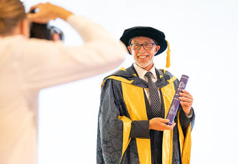 Lloyd Cooke in his graduation cap and gown holding a scroll
