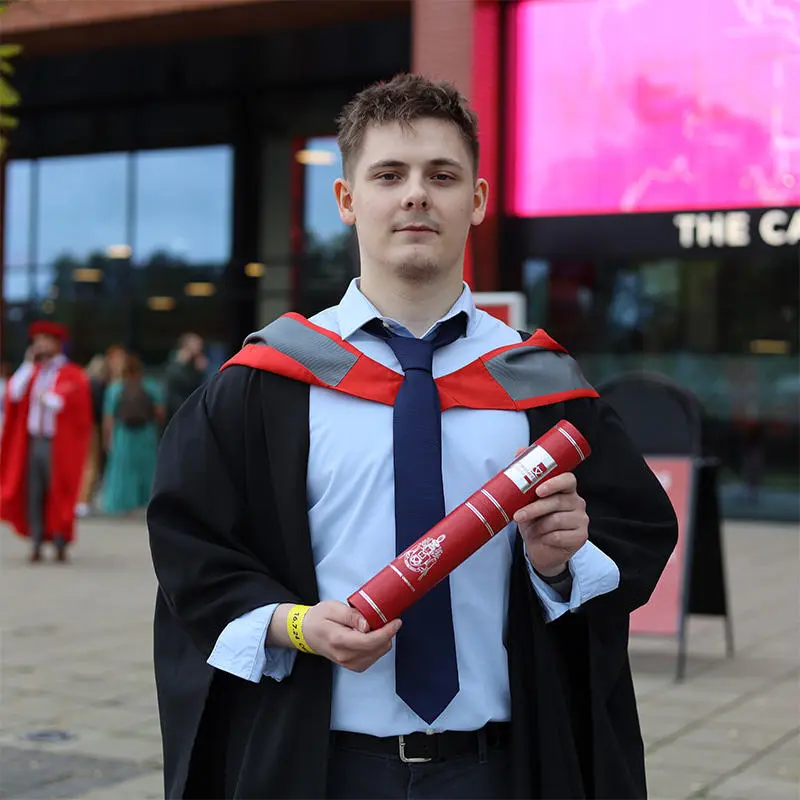 Louis Stonehouse-Gusewski in his graduation gown holding a scroll
