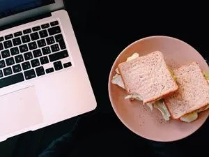 Laptop and a plate of sandwiches sit side by side on a dark desk.