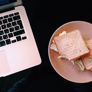 Laptop and a plate of sandwiches sit side by side on a dark desk.