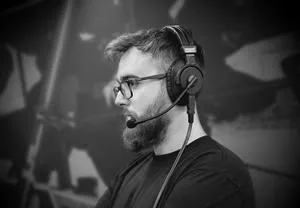 Black-and-white portrait of a bearded man wearing glasses and a headset microphone.