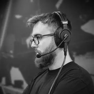 Black-and-white portrait of a bearded man wearing glasses and a headset microphone.