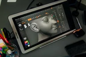 Tablet displays a detailed grey 3D model of a human head in sculpting software.
