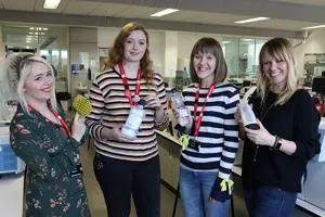Four women in a laboratory hold sample bottles and protective gloves.