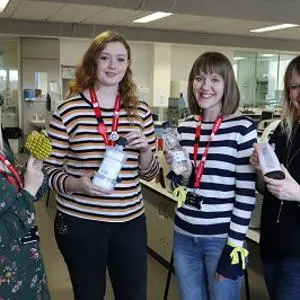 Four women in a laboratory hold sample bottles and protective gloves.