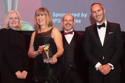Four formally dressed adults pose with a trophy at a university awards ceremony.