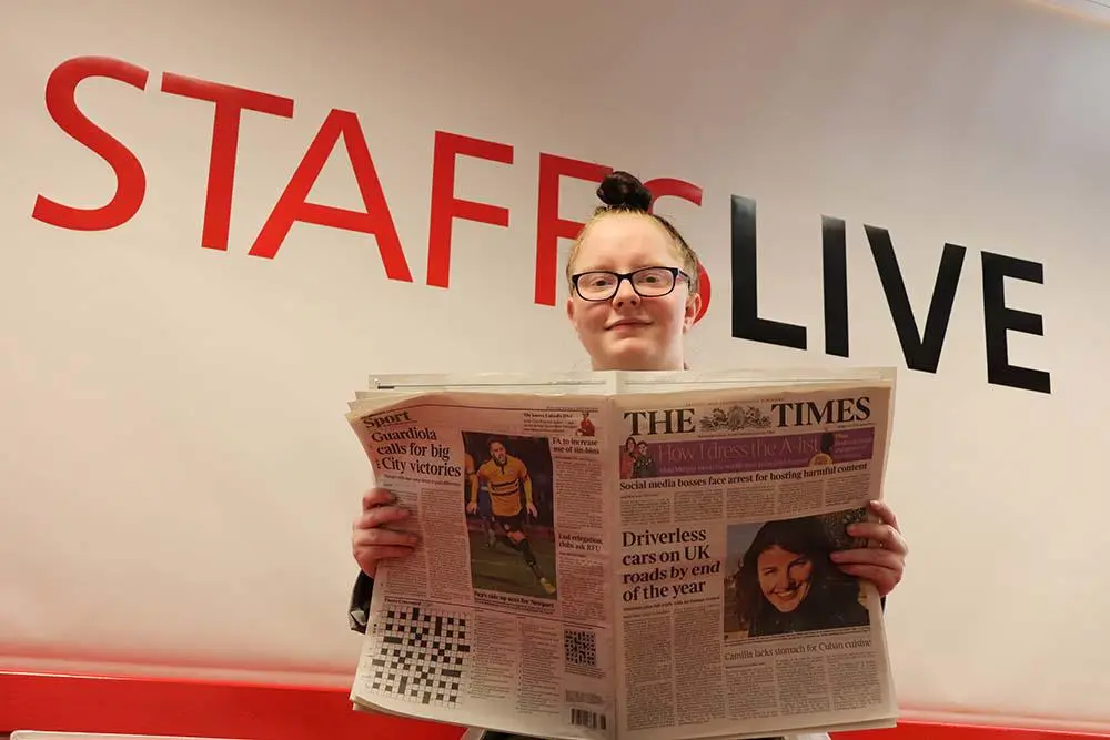 Woman holds an open newspaper beneath large red and black 'STAFFSLIVE' lettering.