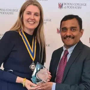 Woman wearing medal presents glass trophy to man in suit