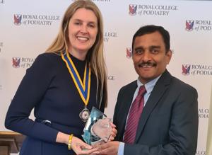 Woman wearing medal presents glass trophy to man in suit