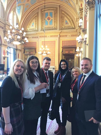 Five people in formal clothing pose inside an ornate government building.