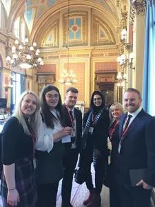 Five people in formal clothing pose inside an ornate government building.