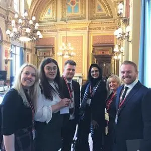 Five people in formal clothing pose inside an ornate government building.