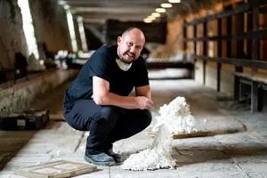 Man crouches beside a white ceramic sculpture inside an abandoned industrial building.