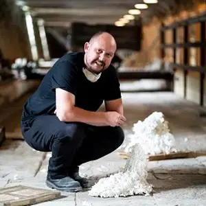 Man crouches beside a white ceramic sculpture inside an abandoned industrial building.