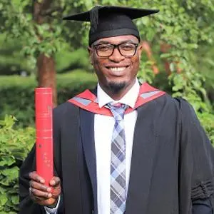 Smiling graduate in cap and gown holds a red diploma tube outdoors.