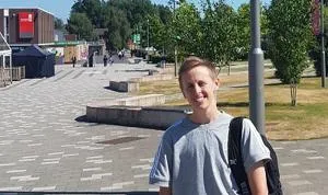 Young man with a backpack stands on a sunny university walkway.