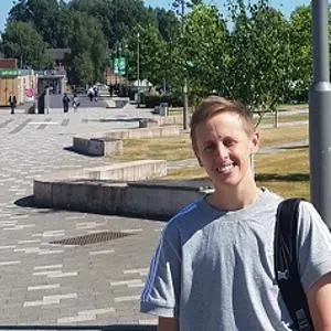 Young man with a backpack stands on a sunny university walkway.