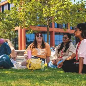 A group of four students sat in front of the Catalyst building on a sunny day