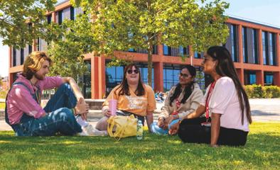 A group of four students sat in front of the Catalyst building on a sunny day