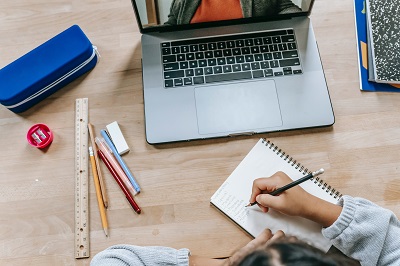 Overhead view of a student writing beside a laptop, ruler, pencils and notebooks.