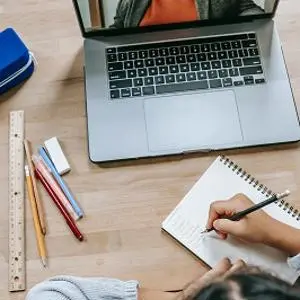 Overhead view of a student writing beside a laptop, ruler, pencils and notebooks.