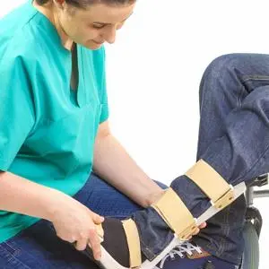 Clinician in green scrubs fits a wooden and fabric orthotic support around a seated person's leg.