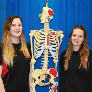 Two smiling women stand on either side of a human skeleton model.