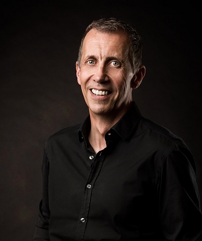 Smiling man in a black shirt poses against a dark studio background.