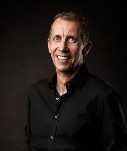 Smiling man in a black shirt poses against a dark studio background.