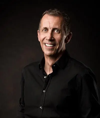 Smiling man in a black shirt poses against a dark studio background.