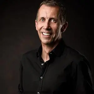 Smiling man in a black shirt poses against a dark studio background.