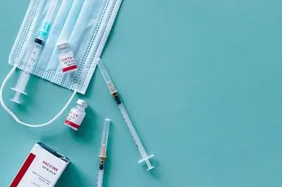 Syringes, surgical masks and vaccine vials arranged on a pale blue surface.
