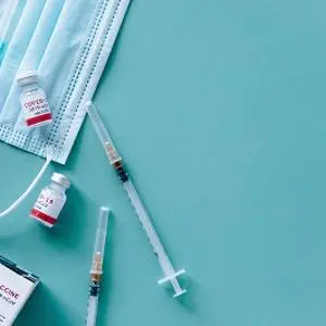 Syringes, surgical masks and vaccine vials arranged on a pale blue surface.
