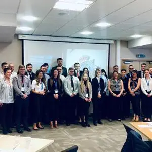 Large group of police recruits and staff poses together in a classroom.