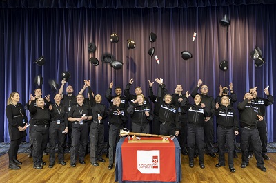 group of 20 police officers celebrating graduation by throwing hats in the air