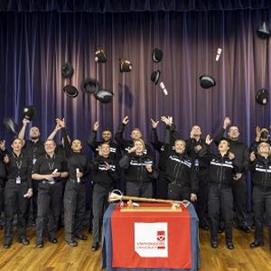 group of 20 police officers celebrating graduation by throwing hats in the air
