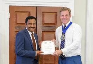 Two men hold a framed certificate during a formal civic presentation.