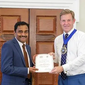 Two men hold a framed certificate during a formal civic presentation.