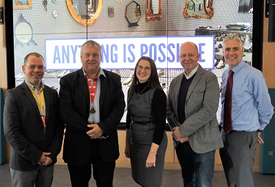 Five adults stand together beneath a large sign reading 'Anything is Possible.'