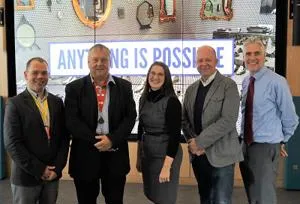 Five adults stand together beneath a large sign reading 'Anything is Possible.'