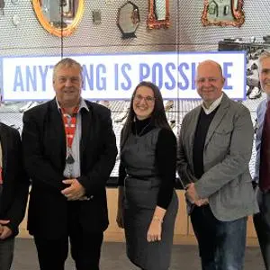 Five adults stand together beneath a large sign reading 'Anything is Possible.'